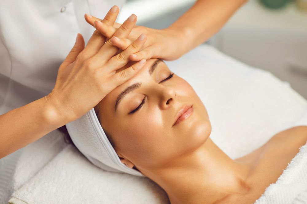 A person receives a relaxing face massage in a dim, candlelit spa setting while lying on a massage table — Soul Good Beauty in Miami, QLD