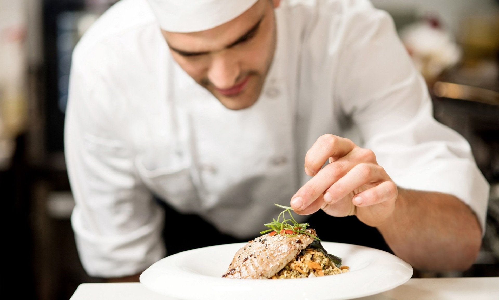 Uno chef guarnisce un piatto con erbe aromatiche nella cucina di un ristorante.
