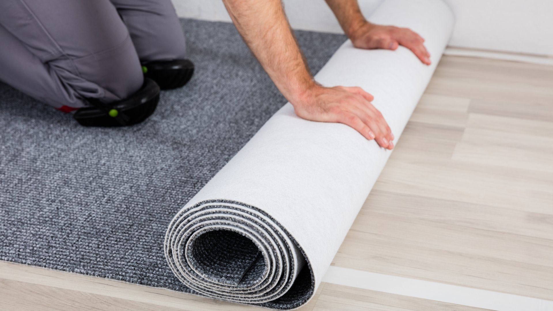 Close-up Of Worker's Hands Unrolling Carpet On Floor At Home