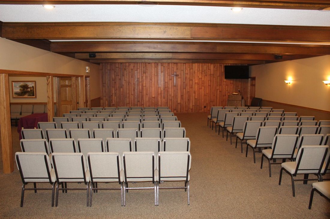 Rows of beige chairs face forward in a room. A table and staircase railing are in the foreground.