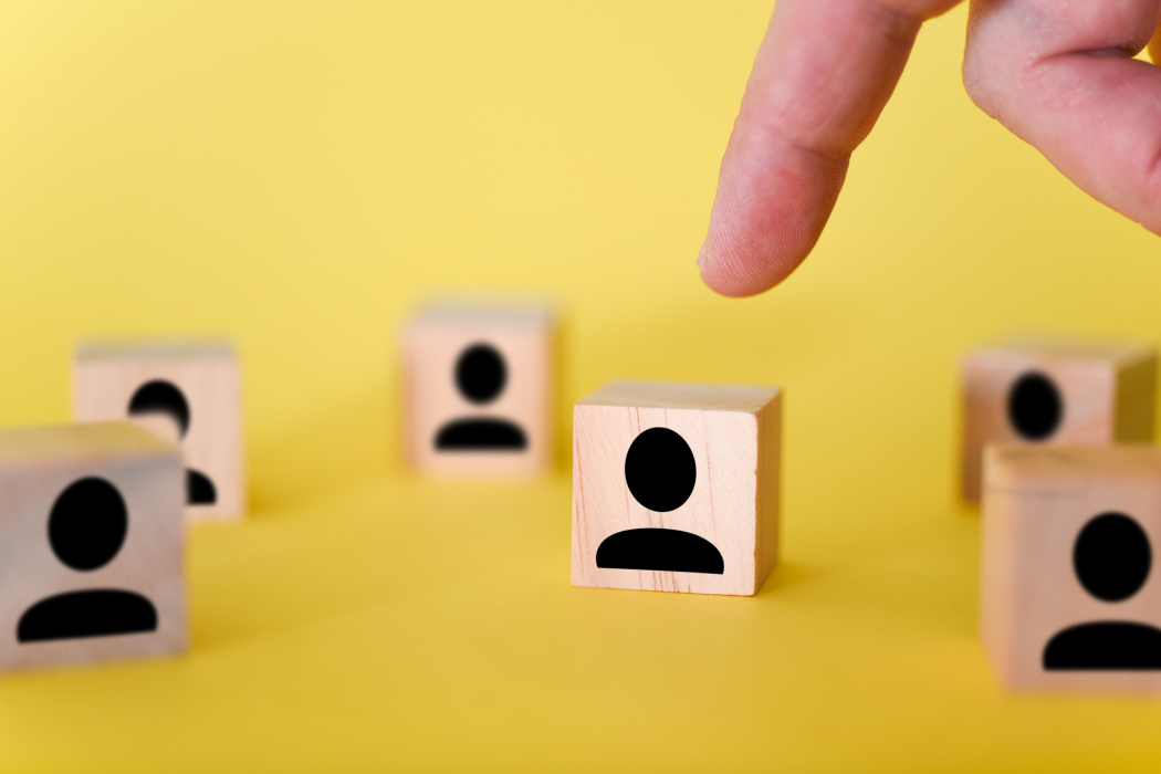 Finger selecting a wooden block with a person icon among others on a yellow surface