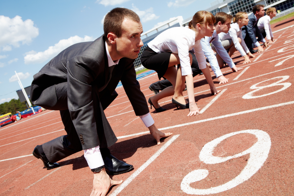 Runners in starting blocks at a track meet, crouched on a red running track with lane numbers visible.