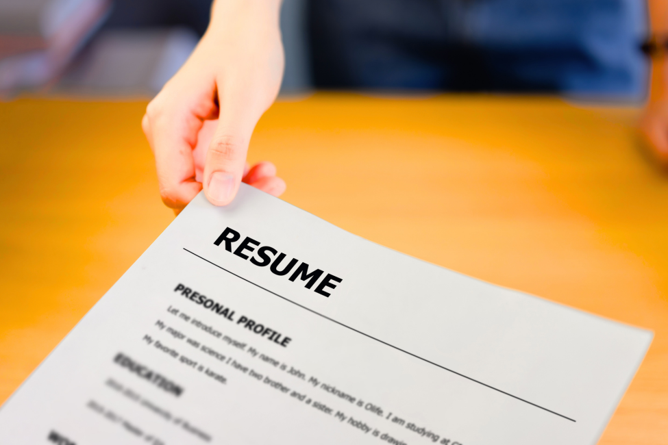 Hand holding a resume document over a wooden desk