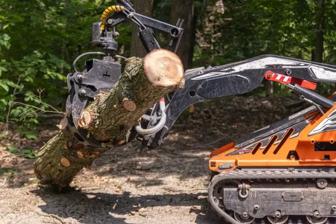 Heavy machinery claw lifting and moving a large log in a wooded area.