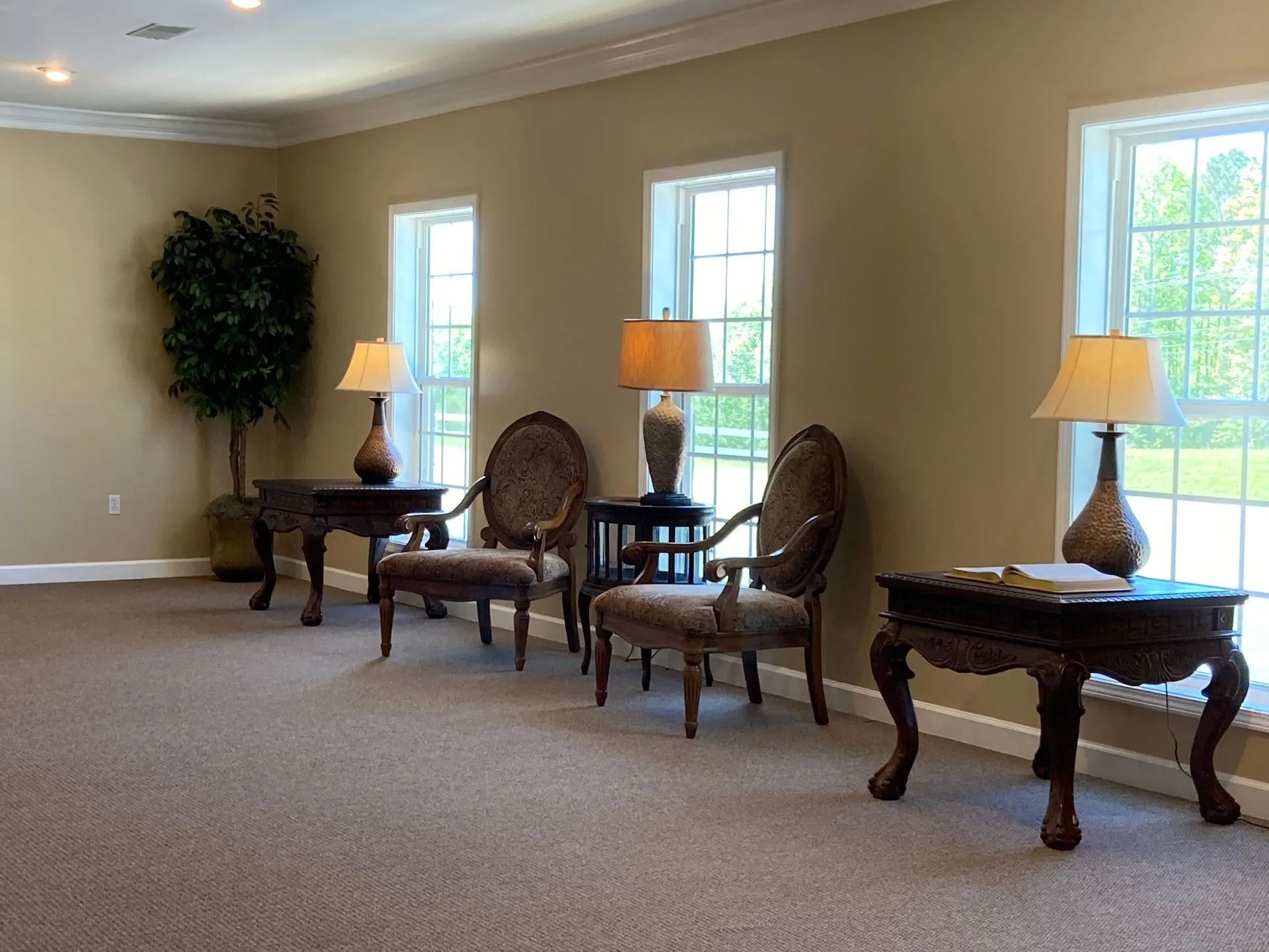 Elegant beige room with three ornate chairs, matching tables, lamps, and tall windows.
