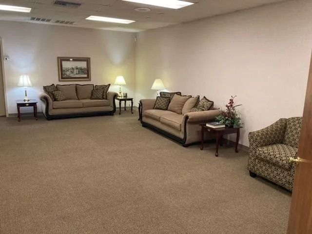 Empty waiting room with beige carpet, sofas, side tables, and soft wall lighting