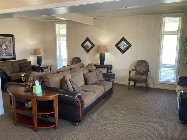 Spacious living room with a brown sofa, side tables, lamps, wall art, and tall windows.