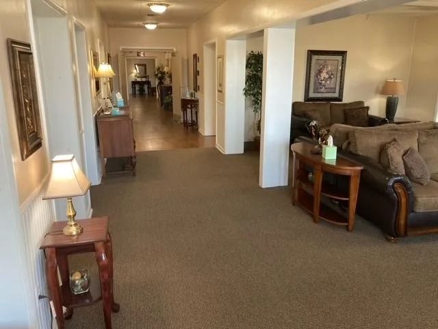 Long hallway in a home with lamps, carpet, and a living room visible on the right.