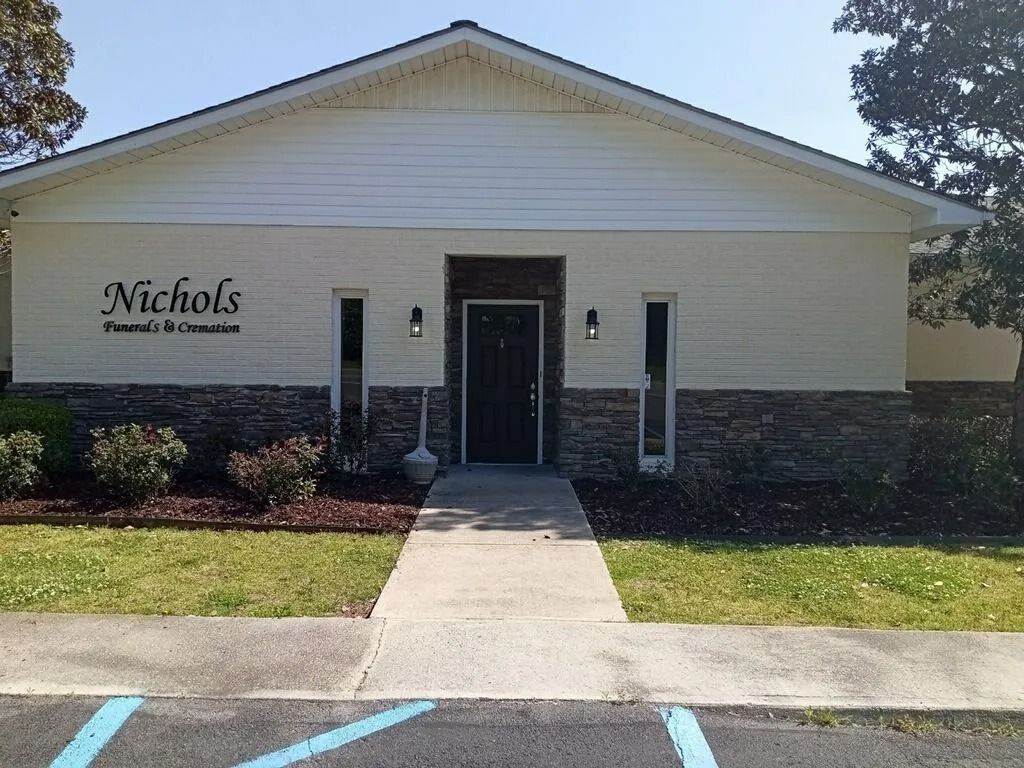Nichols Funeral Home storefront with central entrance, white siding, and a front walkway under a clear sky