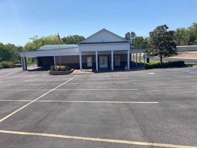 Empty parking lot in front of a small white building with a gabled roof and American flag.