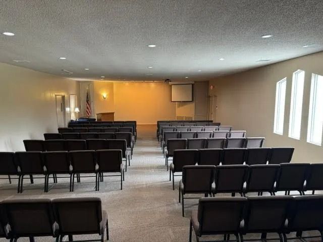 Empty conference room with rows of black chairs facing a projection screen and podium