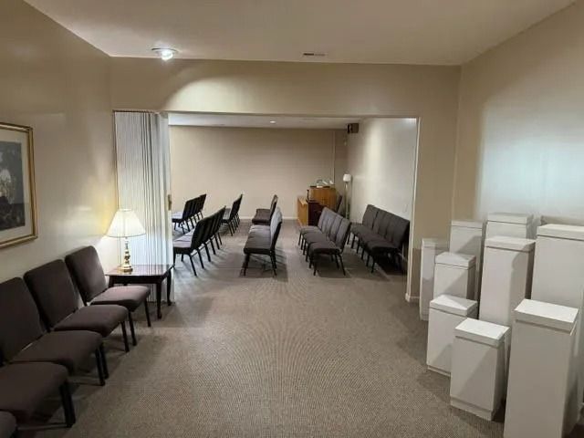 Empty waiting room with rows of chairs, a lamp, and stacked white boxes along the right wall.