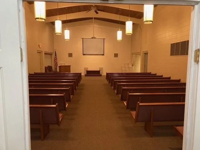 Empty church interior with wooden pews, hanging lights, and an altar at the front