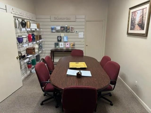Small conference room with a wooden table, burgundy chairs, wall shelves, and framed art.
