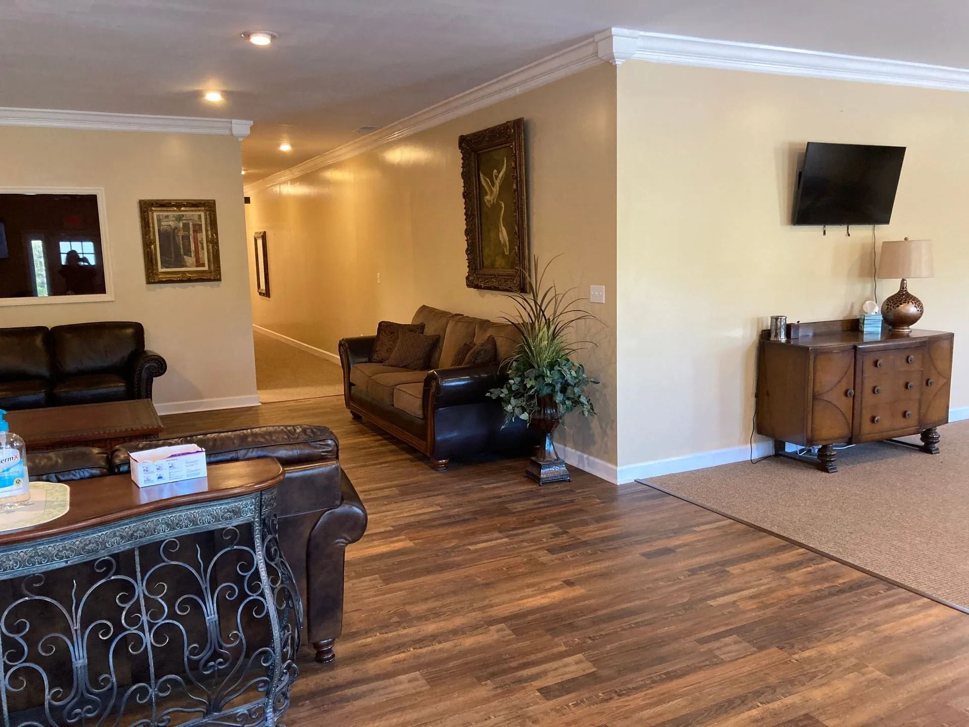 Spacious living room with brown sofas, wood flooring, wall art, and a TV on a cabinet.