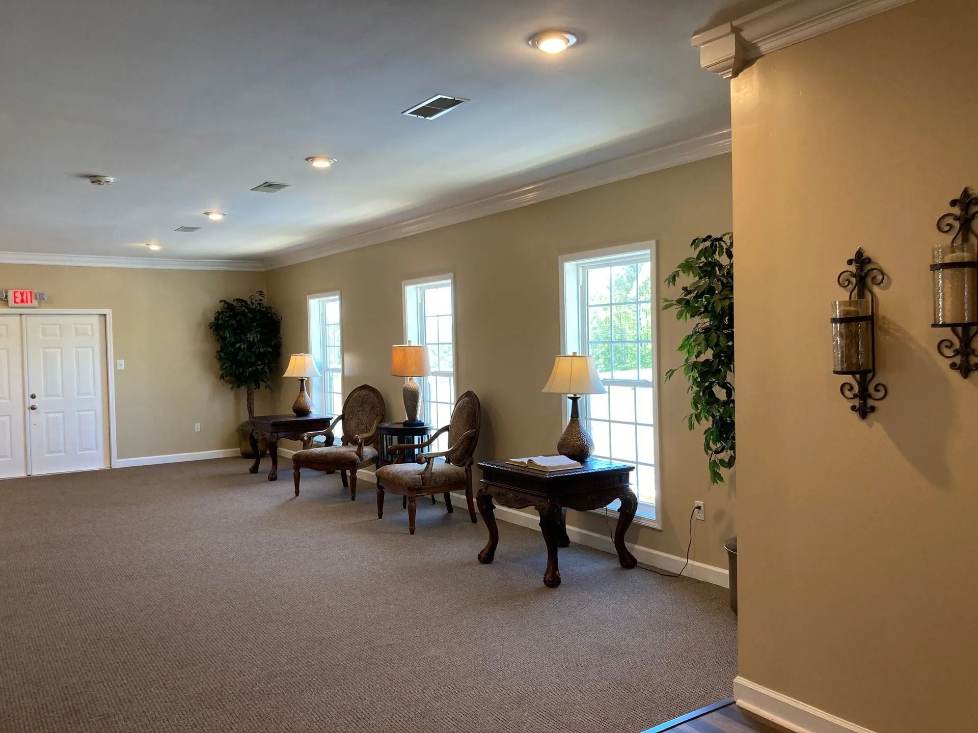 Empty beige lobby with chairs, tables, lamps, windows, and wall decor along the right side