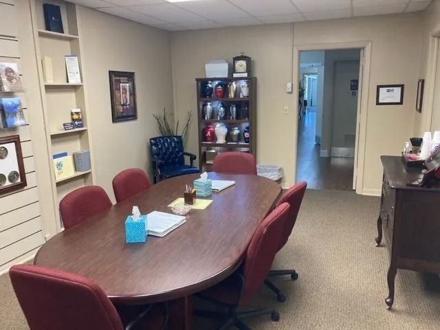 Conference room with oval table, red chairs, shelves, and an open doorway to a hall.