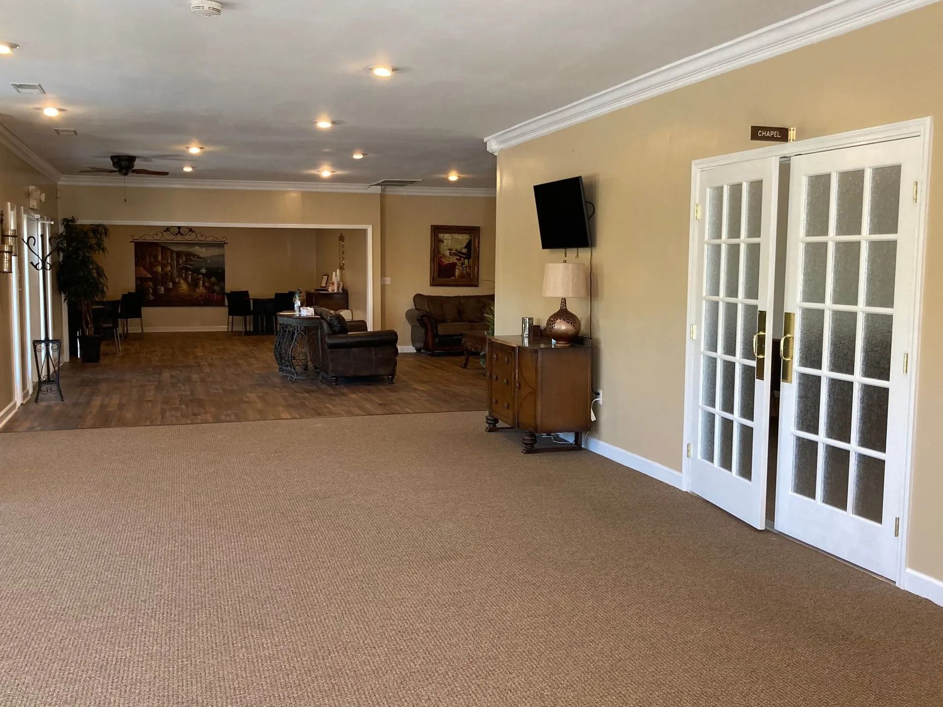Spacious beige lobby with carpet, seating area, wall-mounted TV, and glass doors on the right