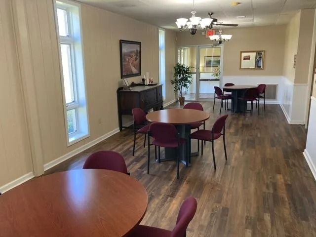 Empty dining room with round wooden tables, maroon chairs, and a large mirror on the wall.