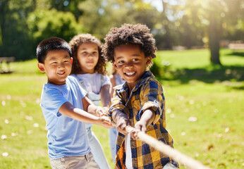 Three young kids are playing tug-o-war in a park. They are smiling.