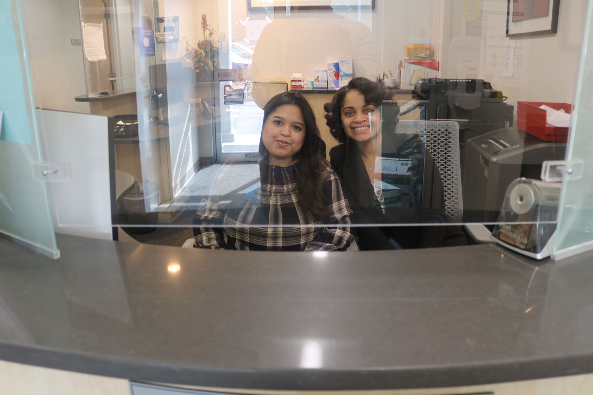 Two people smiling behind a reception desk in an office lobby