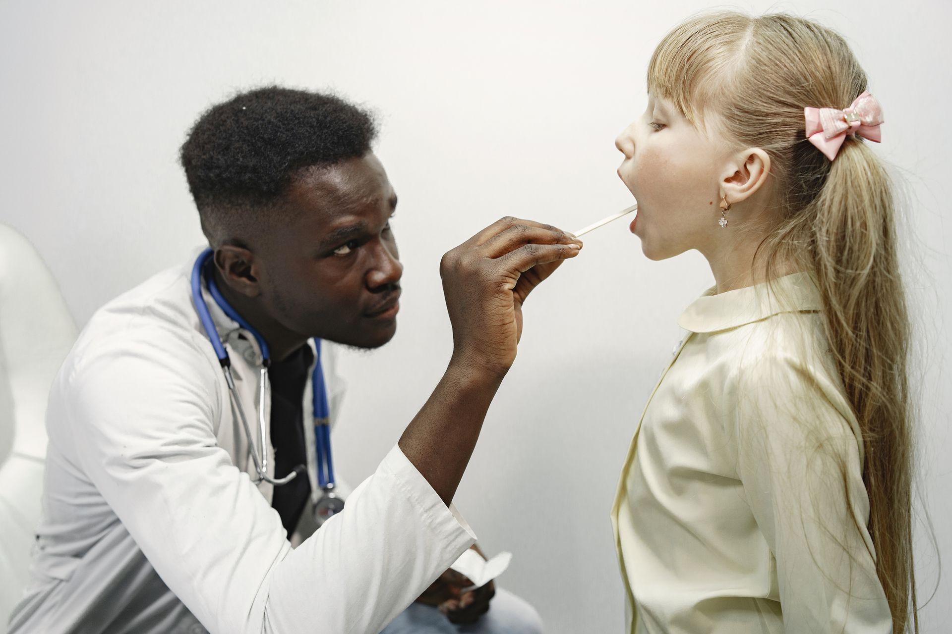 Doctor examining a child’s throat with a tongue depressor in a clinic