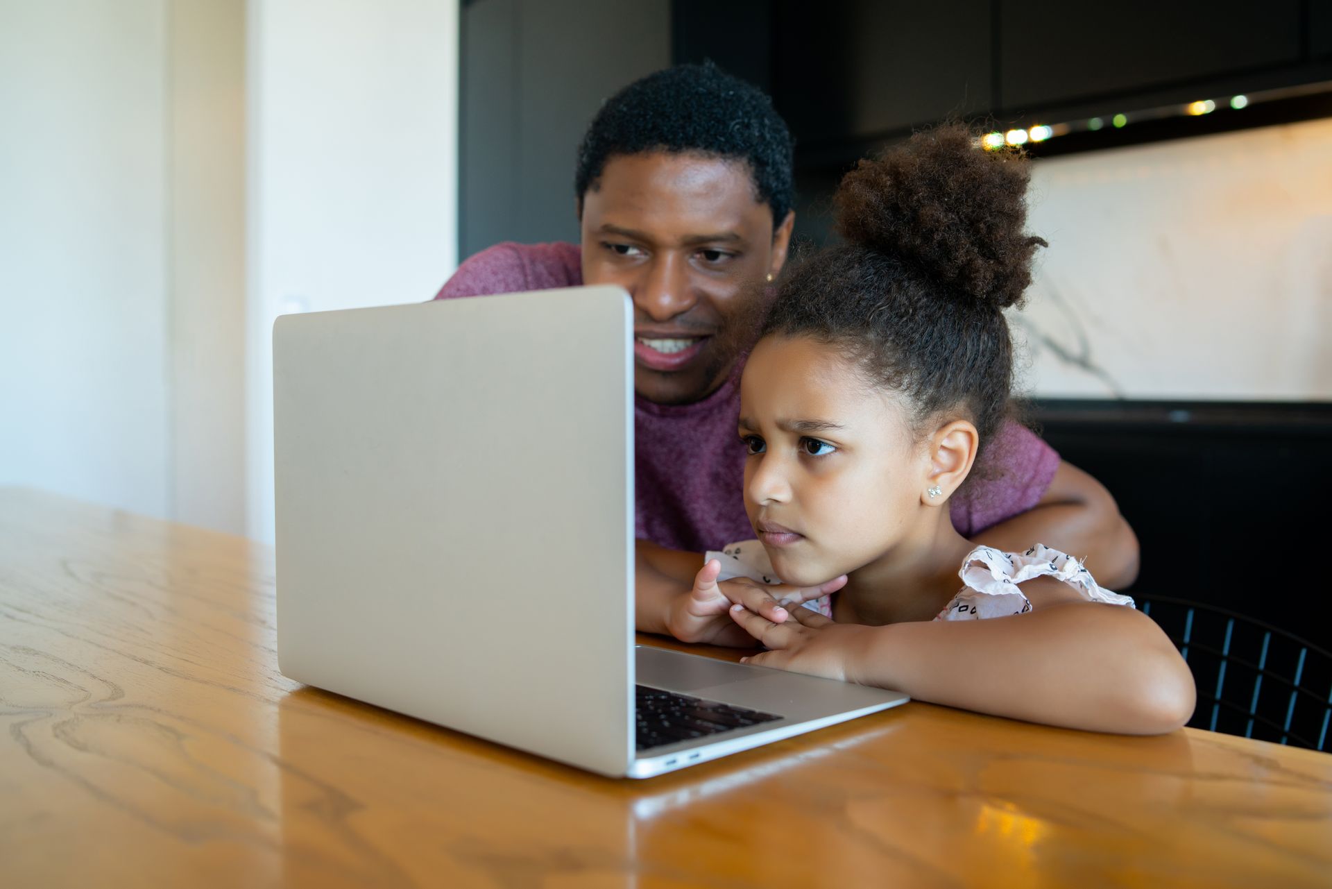 Adult and child using a laptop at a wooden table, both focused on the screen.