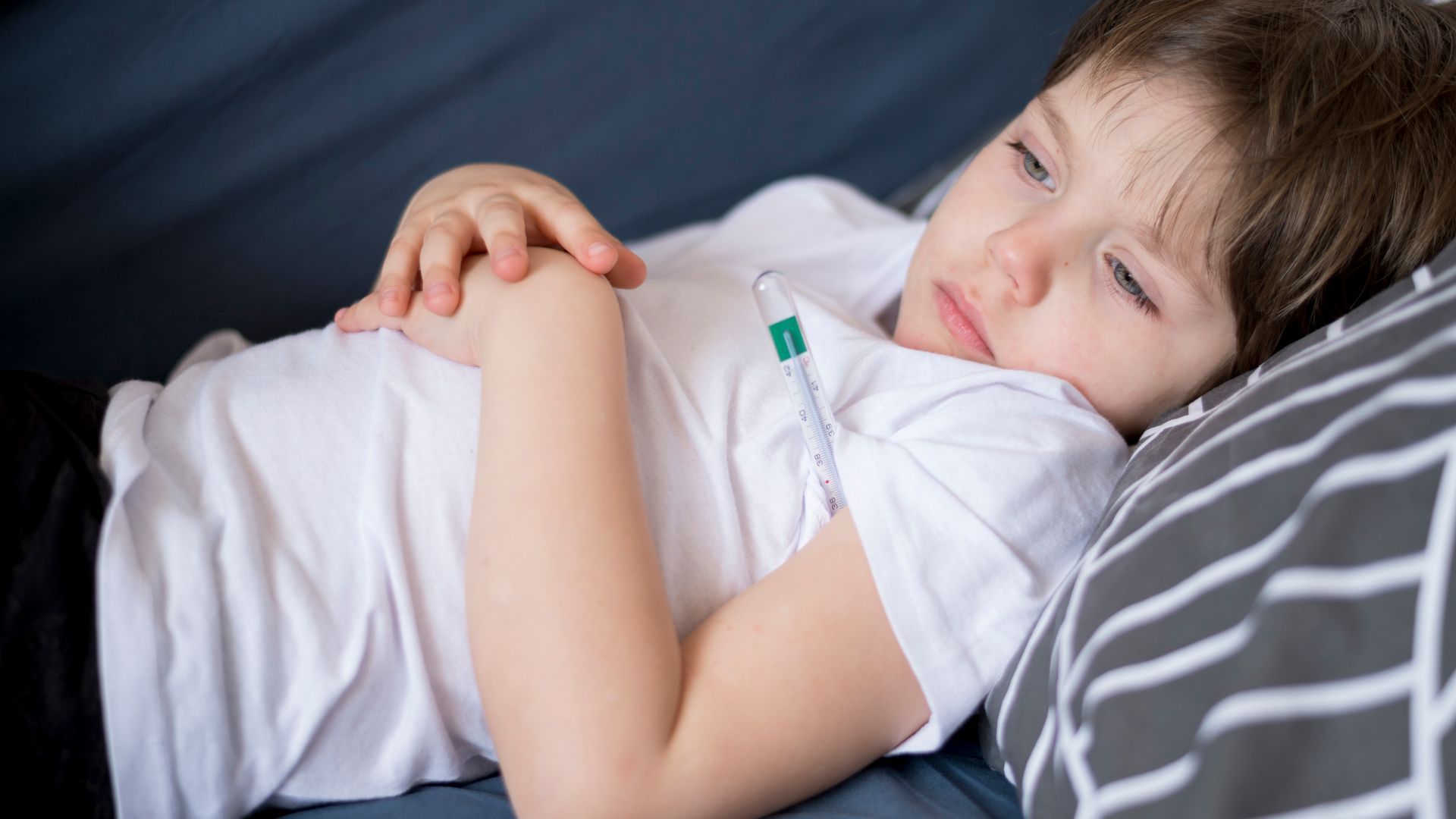 Child sleeping on a couch, hands folded on a white shirt with striped pillow behind.
