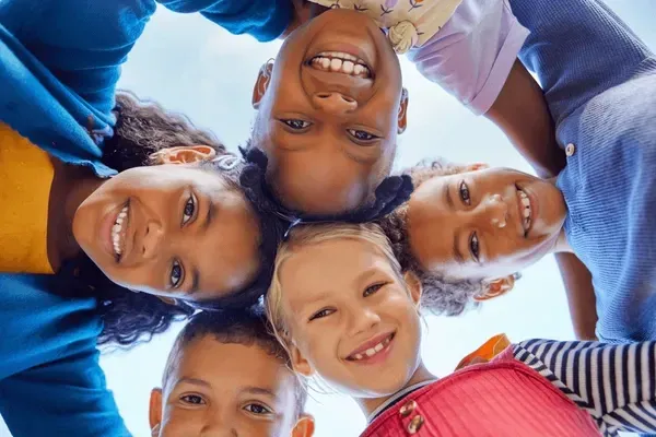 Friends smiling in a circle, looking down at the camera in bright outdoor light.