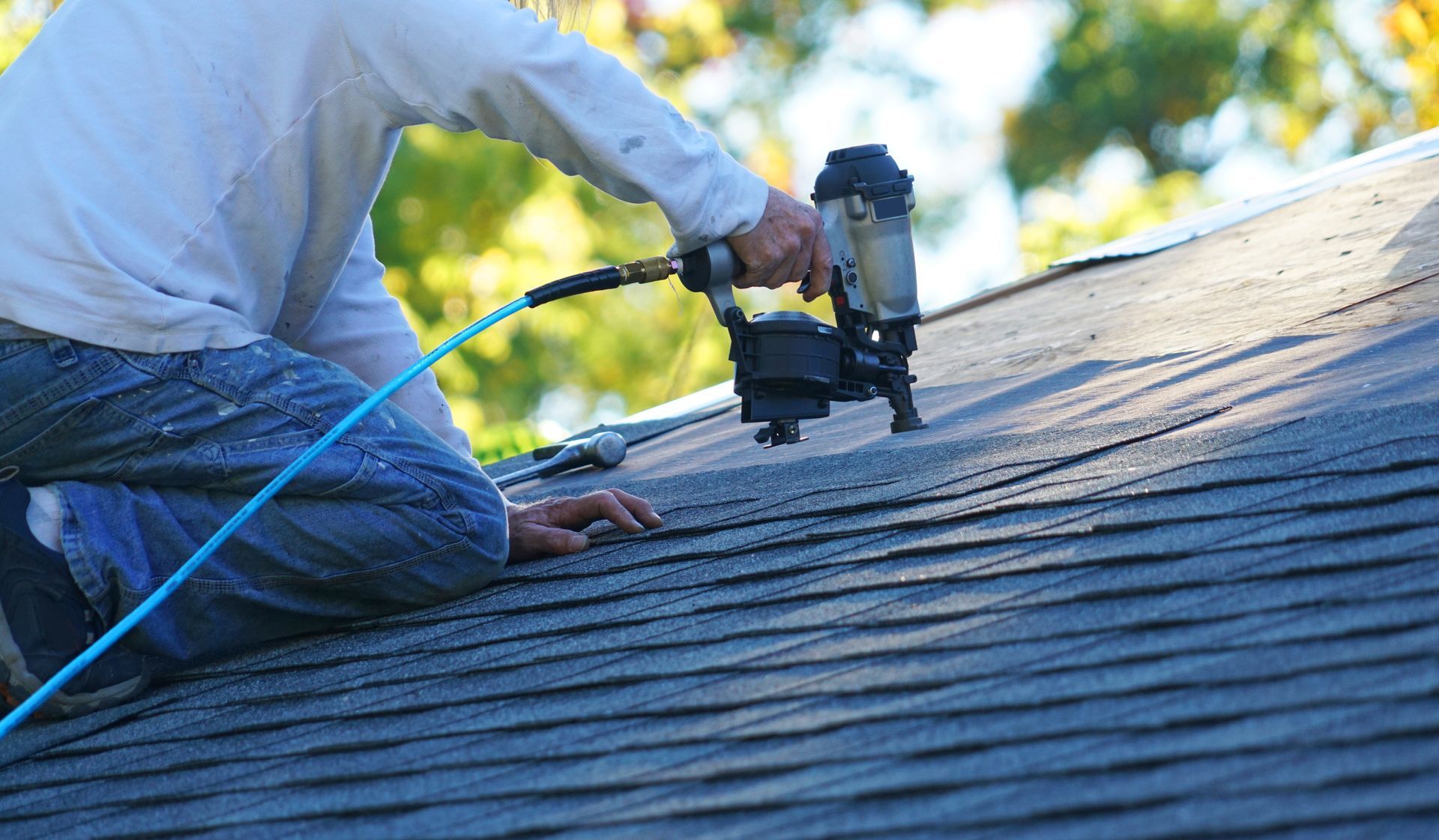Contractor using pneumatic nail gun to install asphalt shingles, securing roofing materials.