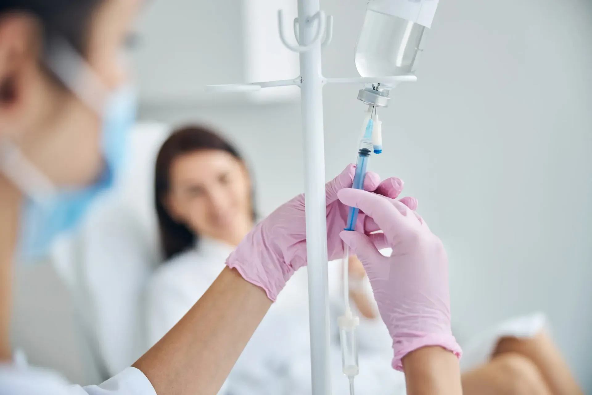 Nurse adjusting IV drip for patient in hospital bed.