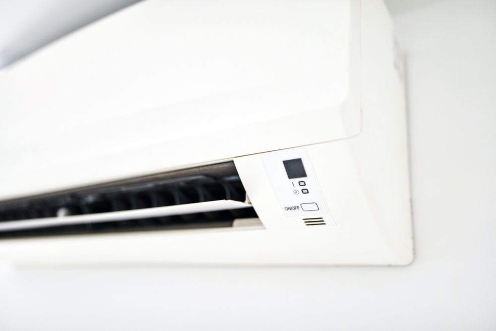 A White Air Conditioner Is Hanging On A White Wall — Air Conditioning Electricians in Harrington, NSW