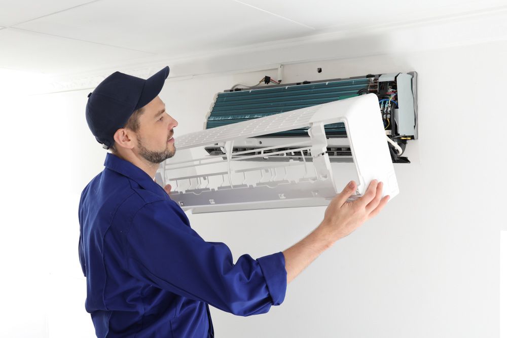 A Man Is Fixing An Air Conditioner On A Wall — Aircon Mid North Coast in Taree, NSW