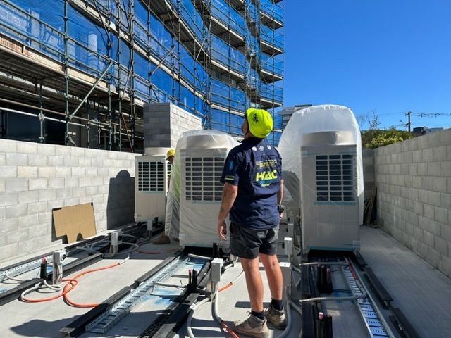 A Man Wearing A Hard Hat Is Standing In Front Of Building Under Construction — Aircon Mid North Coast in Forster, NSW