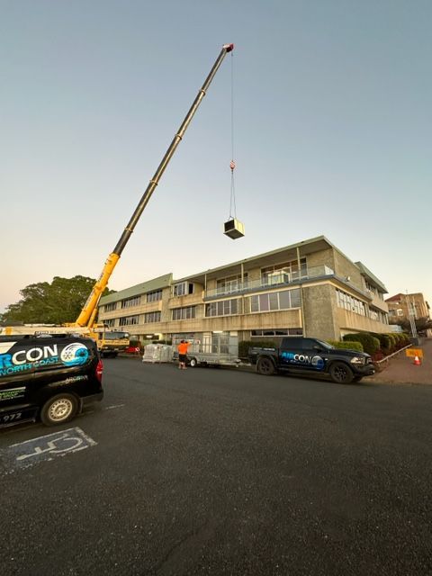 A Crane Is Lifting A Large Object In Front Of A Building — Aircon Mid North Coast in Forster, NSW