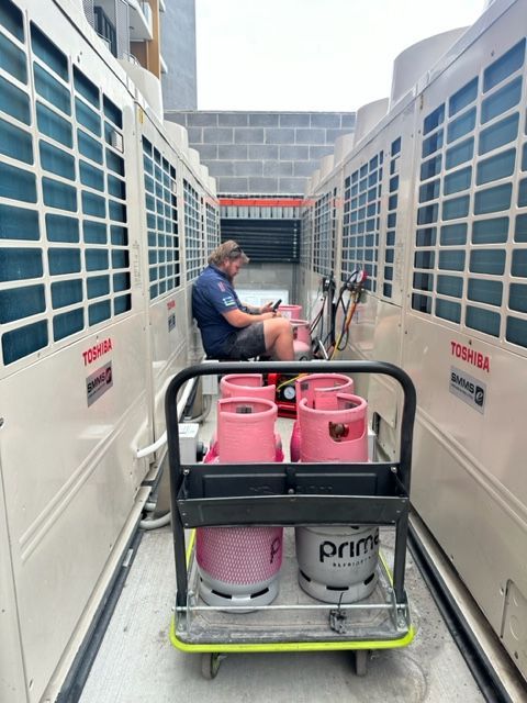 A Man Is Sitting On A Cart With Pink Gas Cylinders On It — Aircon Mid North Coast in Forster, NSW