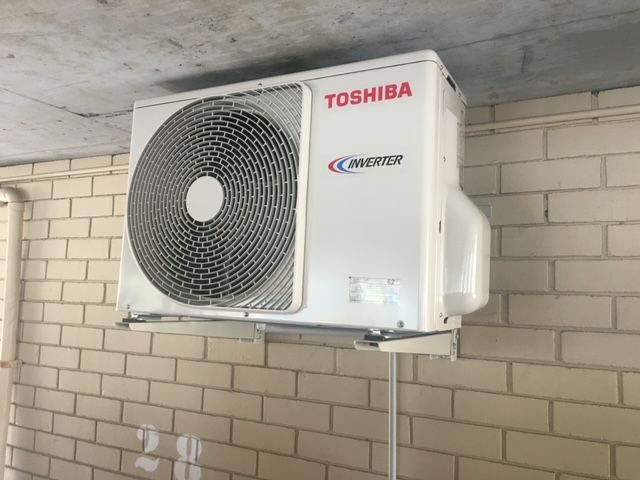 A Toshiba Air Conditioner is Mounted on a Brick Wall — Air Conditioning Electricians in Forster, NSW