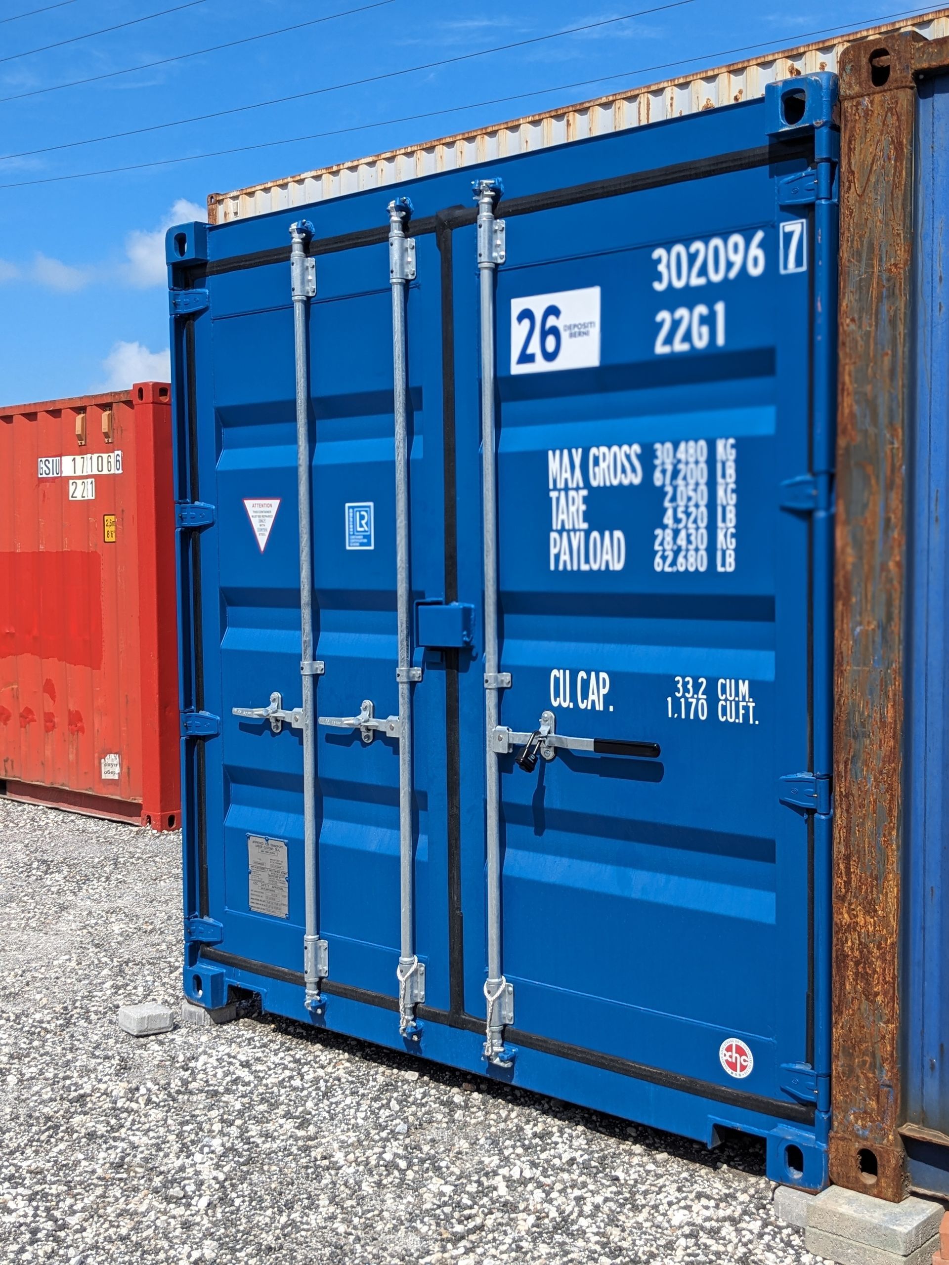 Blue shipping container with white stenciled markings on a gravel lot under a clear sky