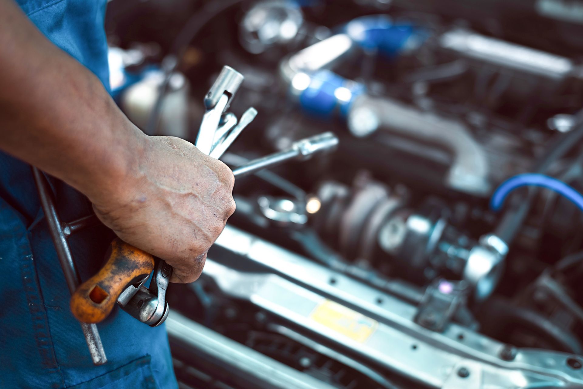 Un meccanico con degli attrezzi in mano, accanto a un motore di un'auto aperto in un'officina.