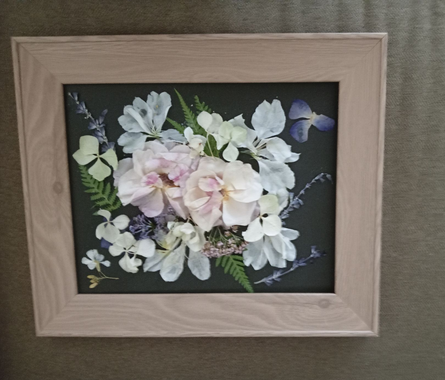 Framed pastel floral arrangement on a dark background, with soft pink, white, and blue flowers.