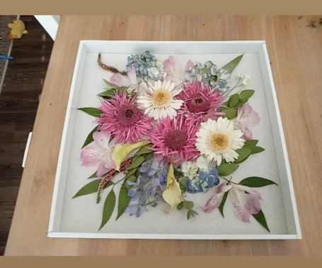 Framed floral wall art with cream, yellow, and orange flowers and green ferns on a textured gray background