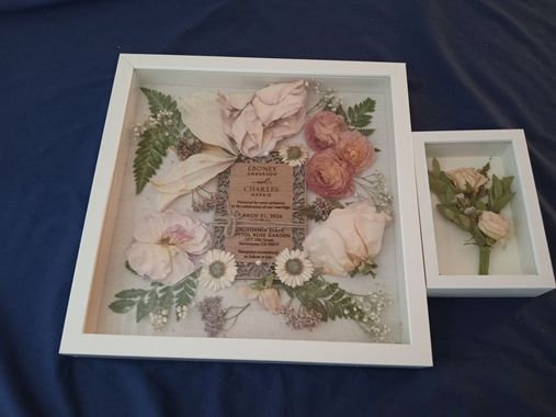 Two framed floral shadow boxes with pastel dried flowers on a blue surface