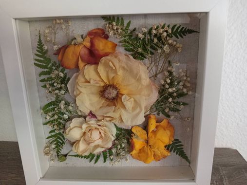Framed floral wall art with cream, yellow, and orange flowers and green ferns on a textured gray background