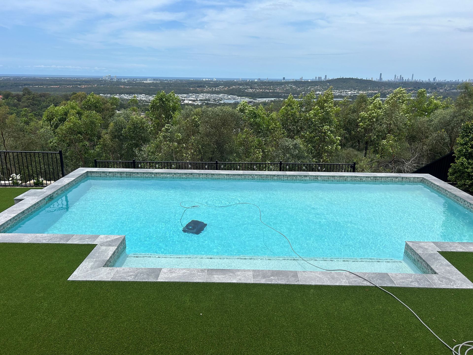 Backyard pool with turquoise water and green lawn, overlooking a distant city skyline