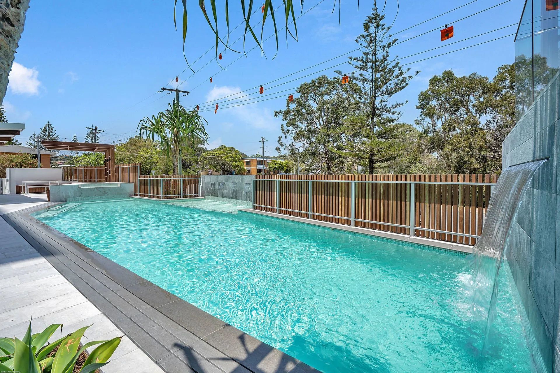 Outdoor swimming pool with turquoise water, wooden fence, and trees under a clear blue sky