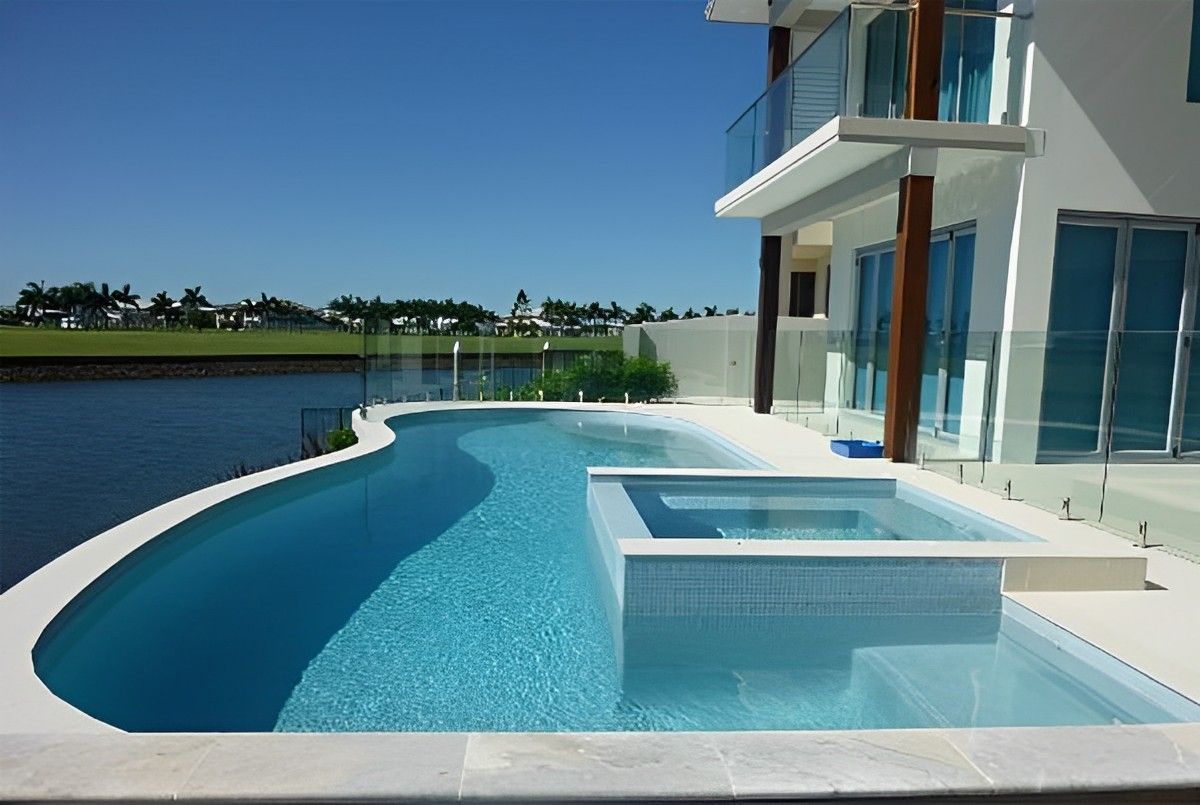Modern white house with a curved blue pool beside a canal under a clear sky
