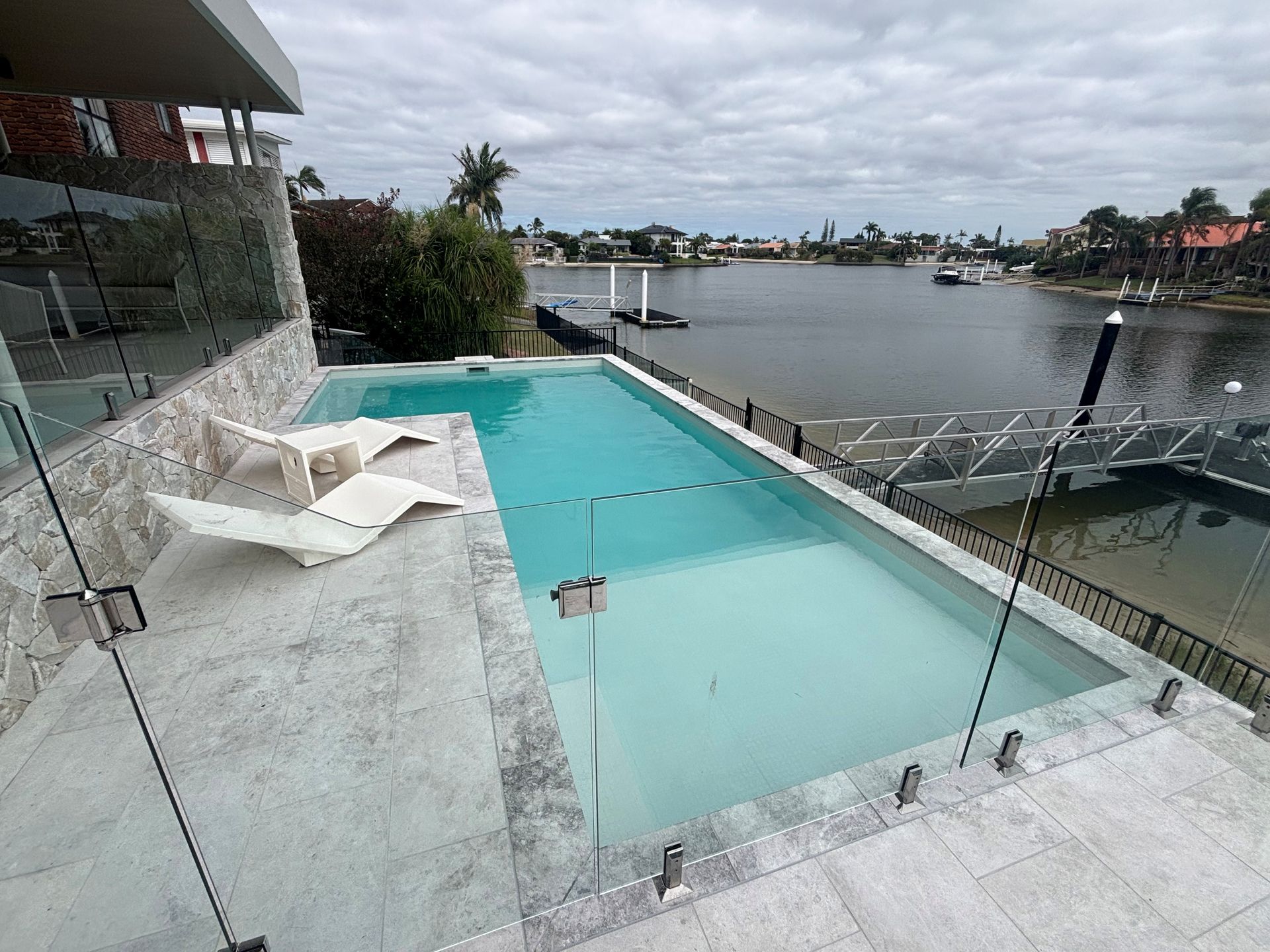 Modern waterfront infinity pool with glass railing overlooking a calm canal at dusk