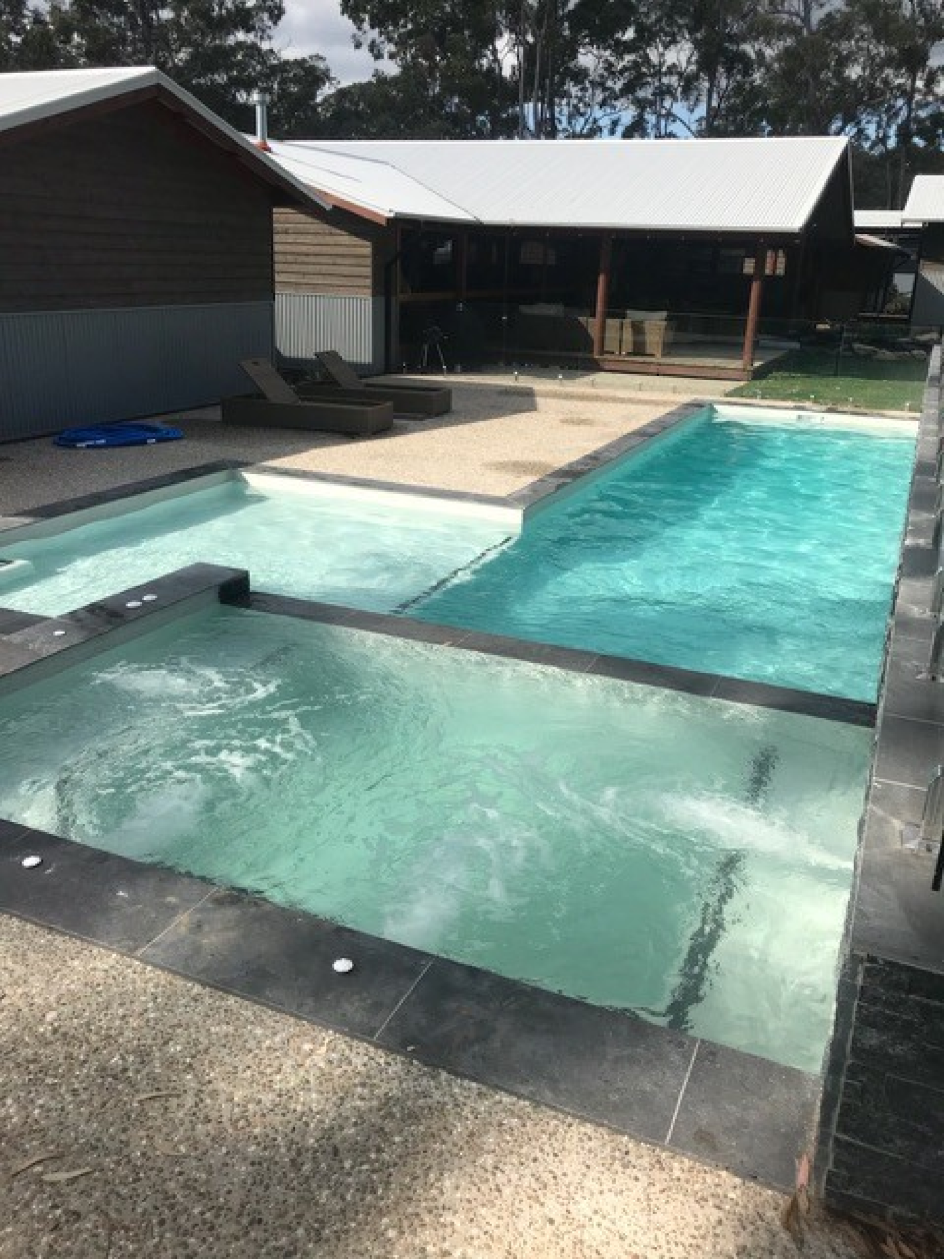 Backyard swimming pool with a shallow ledge, turquoise water, and a covered patio beside it