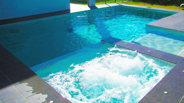 Modern pool with bubbling spa, blue water, and a sunlit patio edge