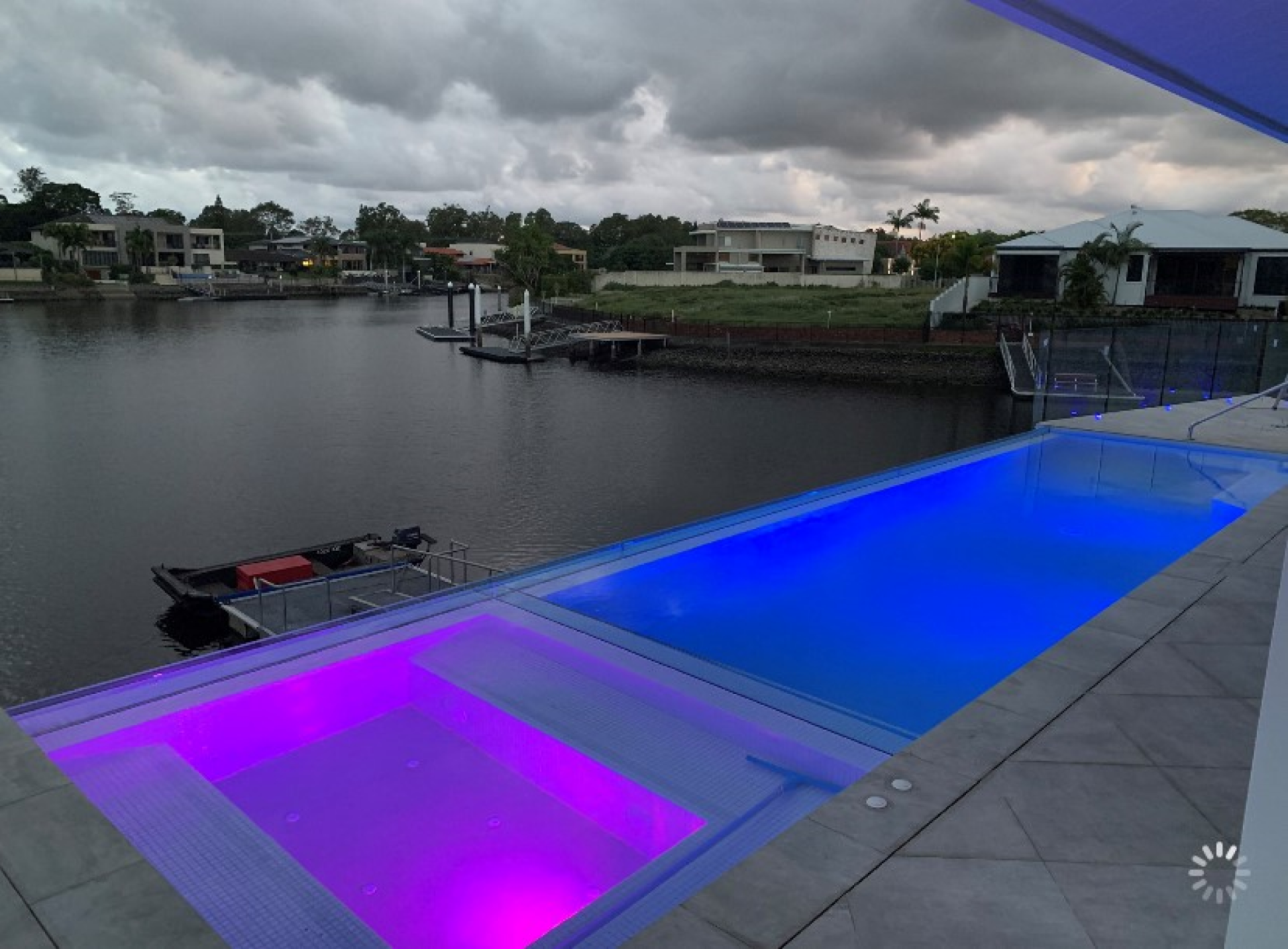 Canal at dusk with glowing blue and purple pool lights beside a dock and waterfront homes